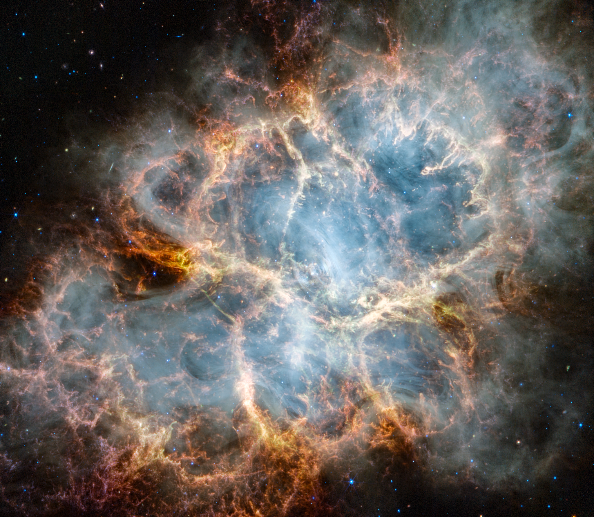 The Crab Nebula is an oval nebula with complex structure against a black background. On the nebula’s exterior, particularly at the top left and bottom left, lie curtains of glowing red and orange fluffy material. Its interior shell shows large-scale loops of mottled filaments of yellow-white and green, studded with clumps and knots. Translucent thin ribbons of smoky white lie within the remnant’s interior, brightest toward its center. The white material follows different directions throughout, including sometimes sharply curving away from certain regions within the remnant. A faint, wispy ring of white material encircles the very center of the nebula. Around and within the supernova remnant are many points of blue, red, and yellow light.