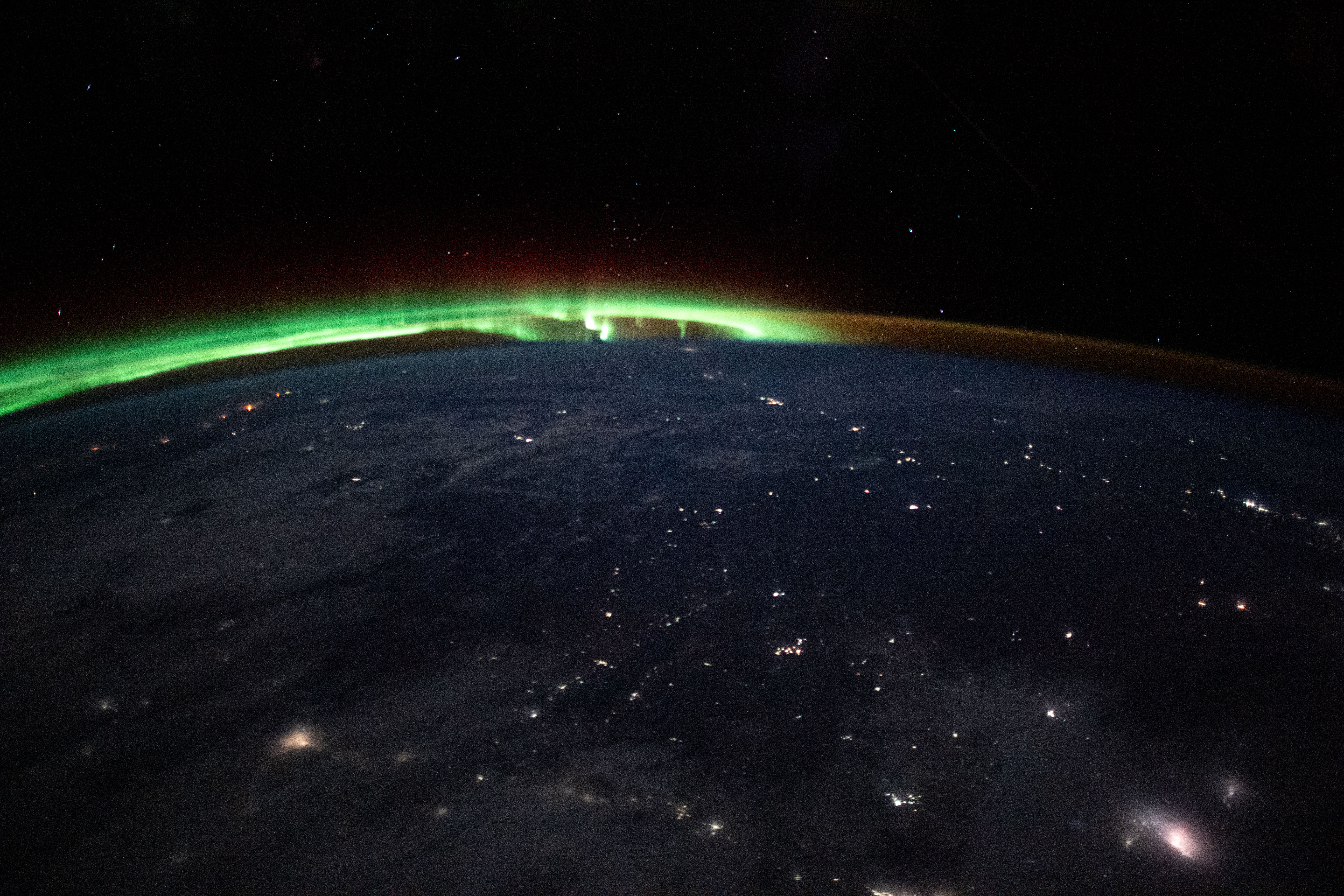 iss070e028203 (Nov. 21, 2023) -- An aurora dances in the horizon of Earth's atmosphere as city lights shine through clouds cast over Mongolia while the International Space Station orbited 263 miles above.