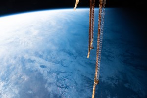 iss070e029761 (Nov. 24, 2023) -- As the International Space Station begins to enter orbital nighttime 262 miles above the Tian Shan mountain range, clouds hang over the glaciated region. The golden hue of three of the station's solar arrays contrasts the backdrop of Earth's blue glow near the center-right of the image.