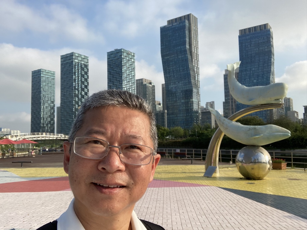 Tony Kim standing in front of a statue of a Whale on a large metal ball in South Korea's Songdo Central Park.