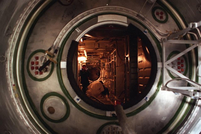 Commander Bill Shepherd of the first International Space Station crew is visible as he inspects the interior of the Russian Service Module recently at the Khrunichev Space and Rocket Center factory in Moscow. The Service Module will be the first fully Russian contribution to the station when it is launched on a Russian Proton booster in December 1998. It will be the cornerstone of the early station, providing living quarters, data processing systems, power, propulsion and life support systems. This view is looking in the aft hatch of the module through the cylindrical transfer chamber into the main compartment. Shepherd's crew will be launched in January 1999 for a five-month stay on the station and includes cosmonauts Yuri Gidzenko, Soyuz Commander, and Sergei Krikalev, Flight Engineer. The crew will fly to the station aboard a Russian Soyuz spacecraft.