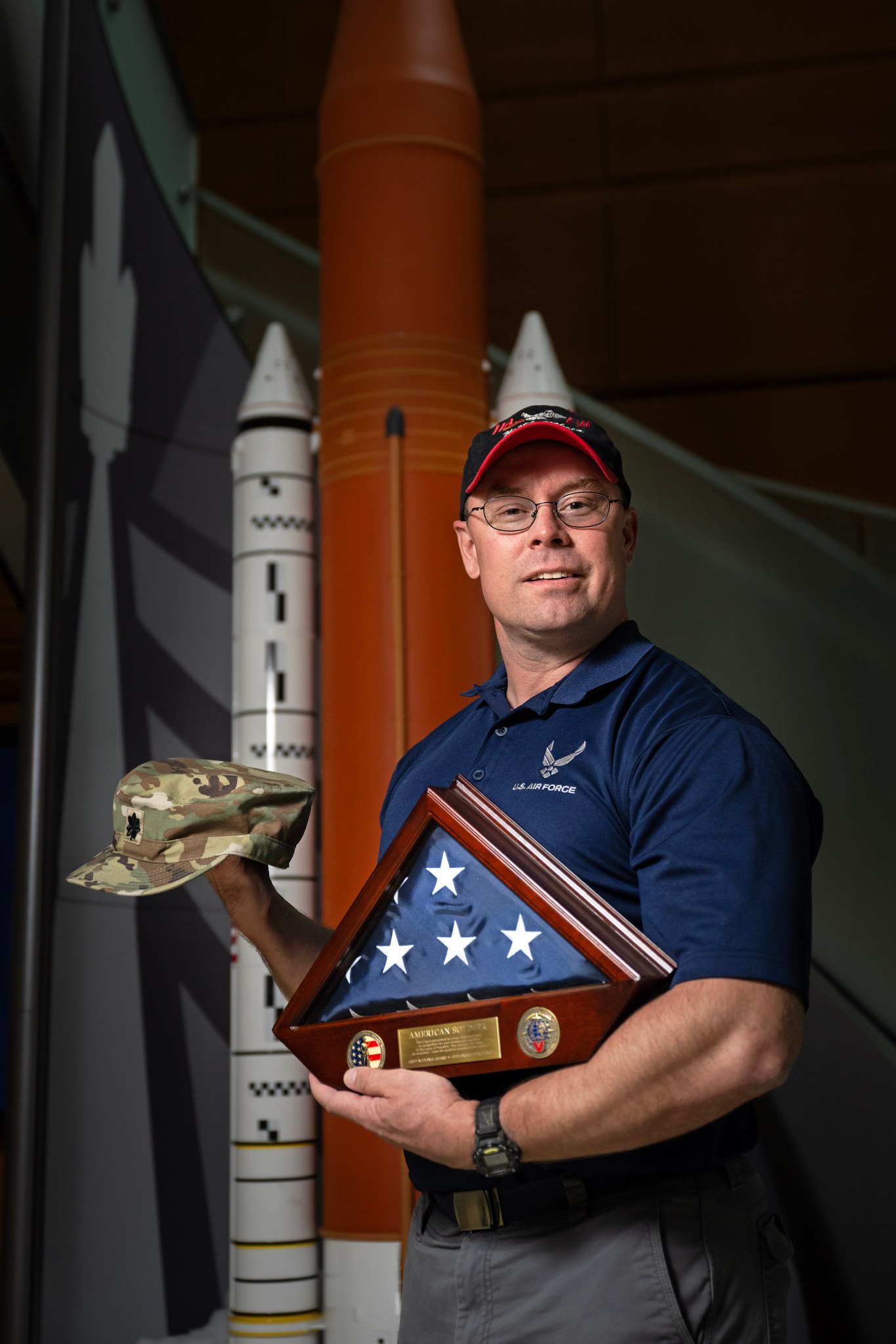 A white man stands in front of a model SLS with his American flag in a wooden box.