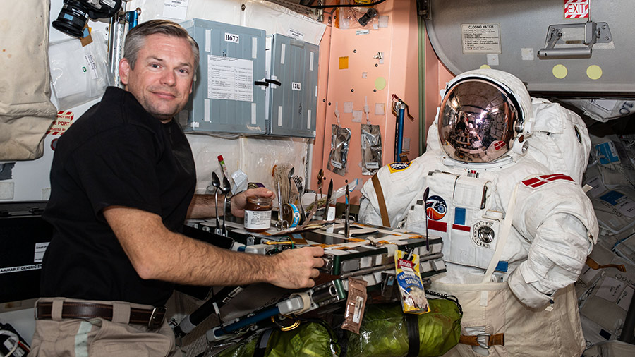 Astronaut Andreas Mogensen poses for a playful portrait with an empty spacesuit across from him inside the Unity module's galley.