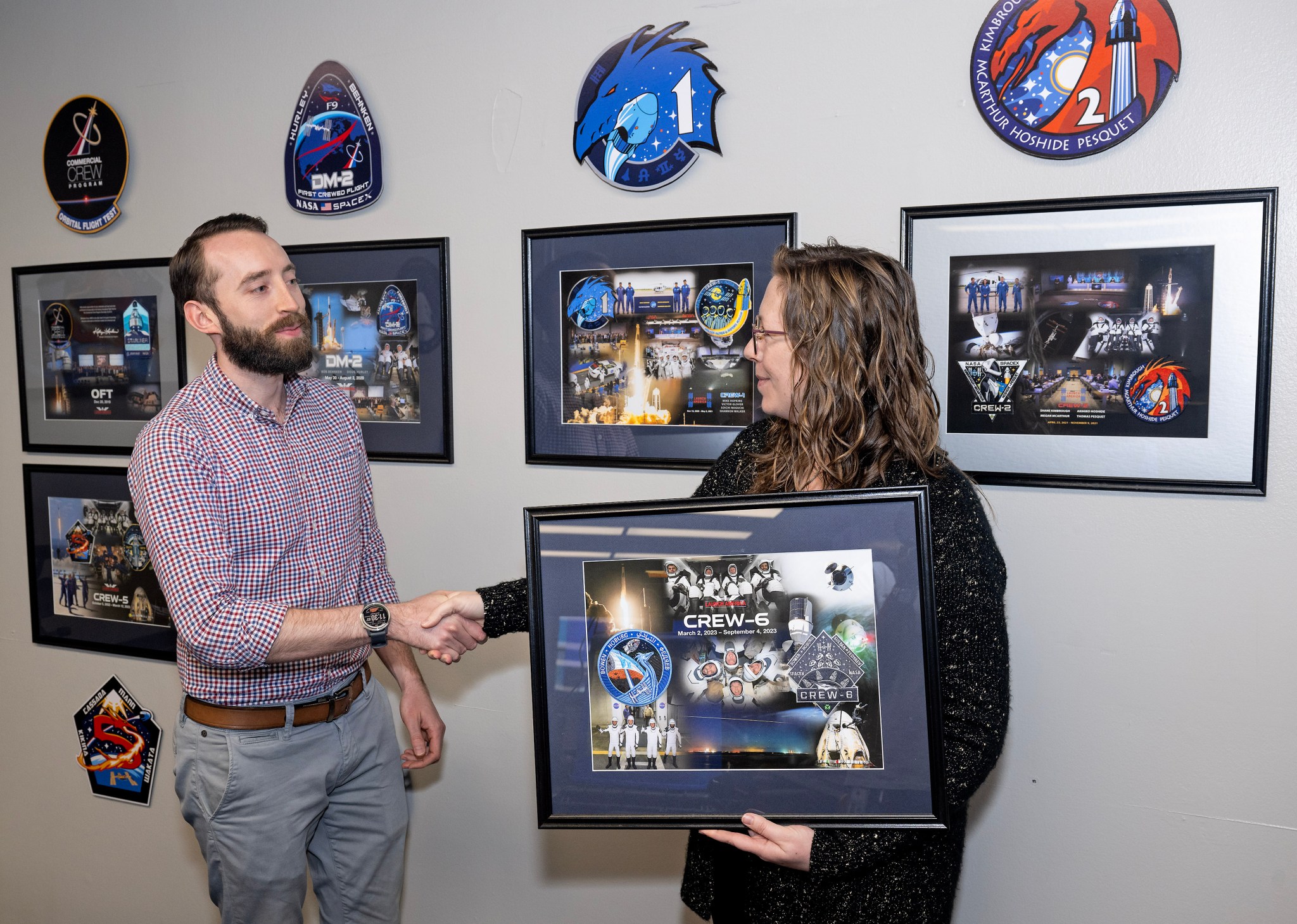 Jonathan Carman, left, deputy SpaceX Falcon 9 lead engineer, shakes hands with McCollum before he hangs the Crew-6 mission plaque.