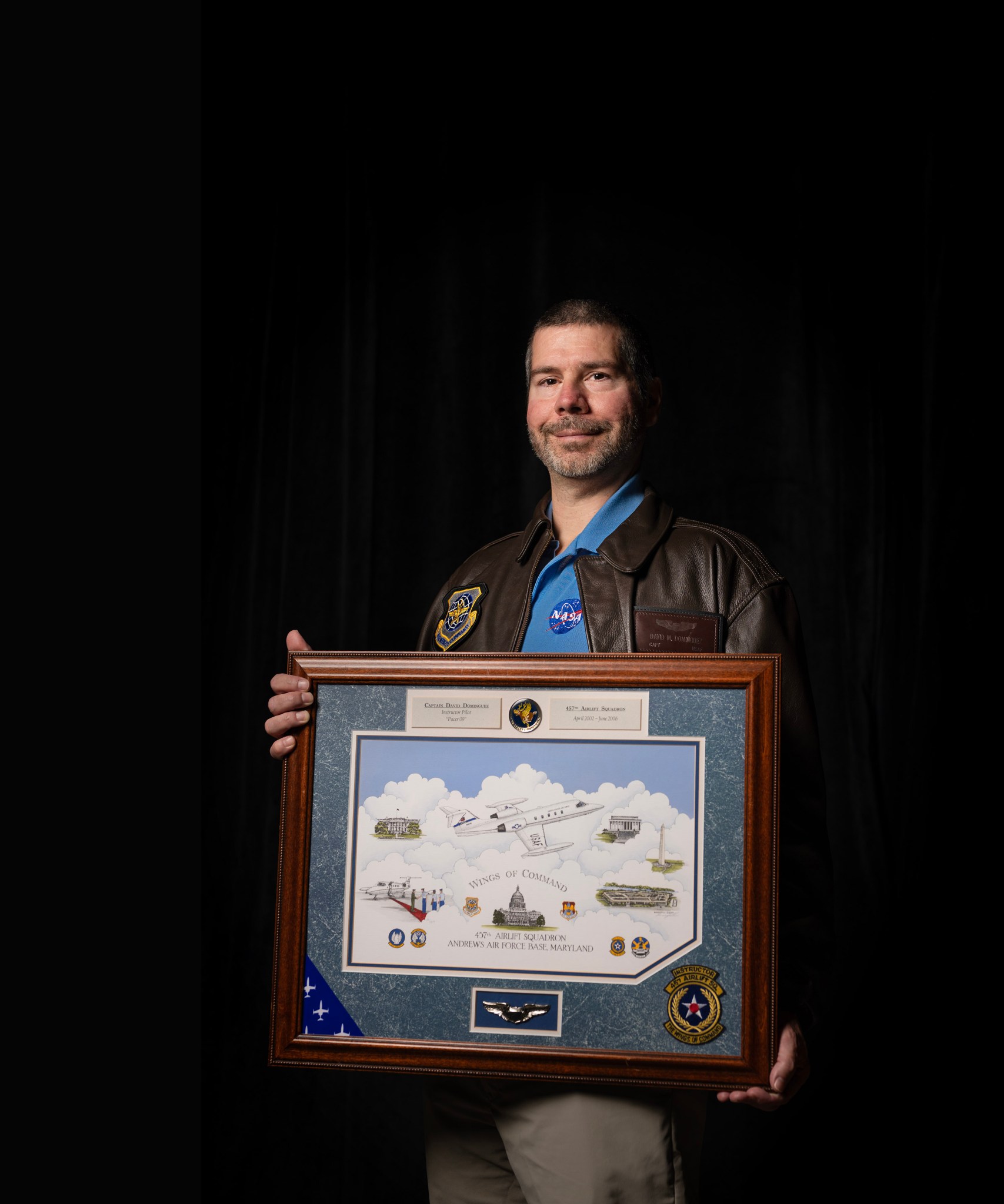 A man stands in a leather jacket holding a shadow box.