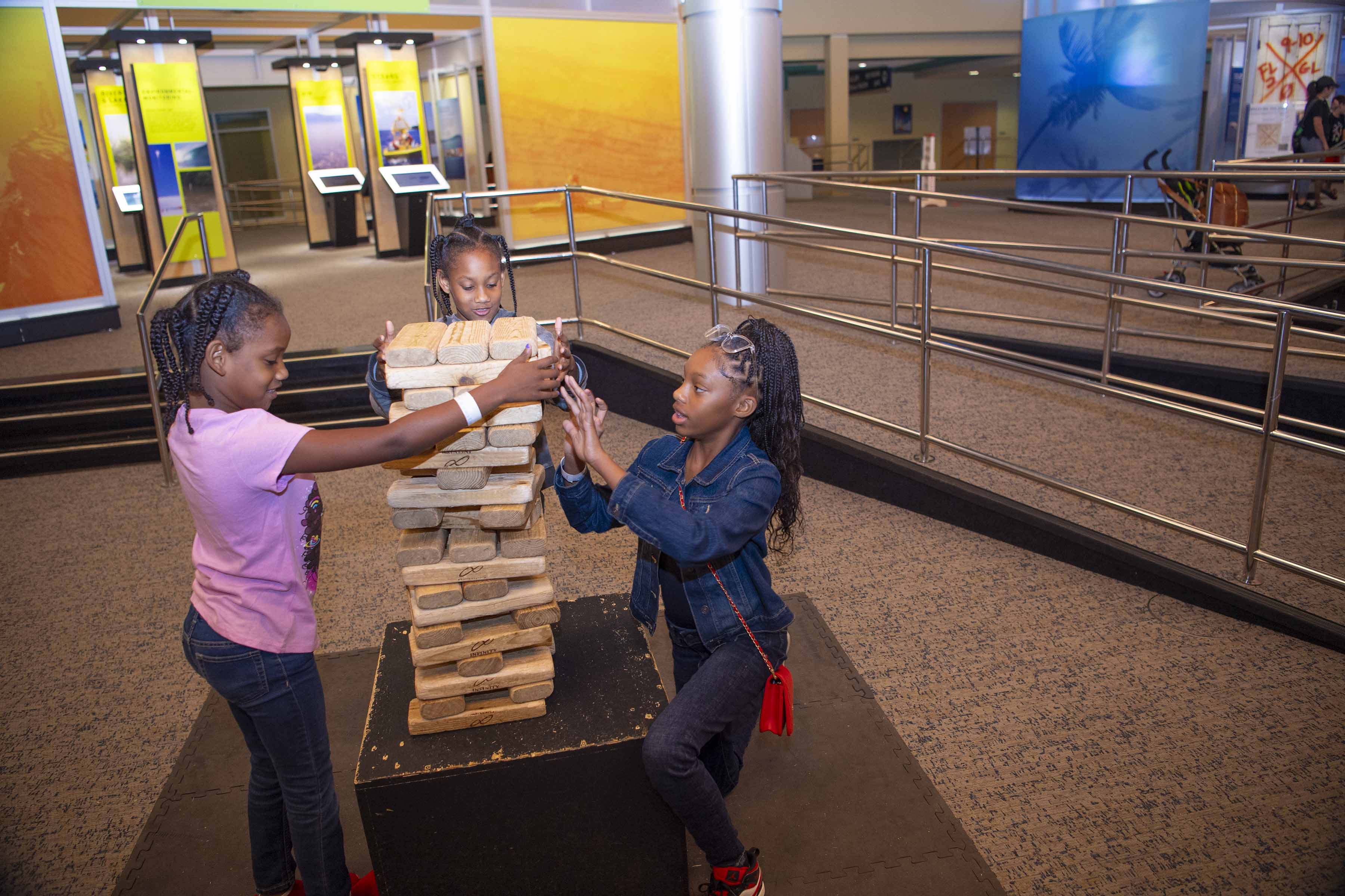 Three young visitors take turns removing pieces of wood from the giant-size blocks puzzle.