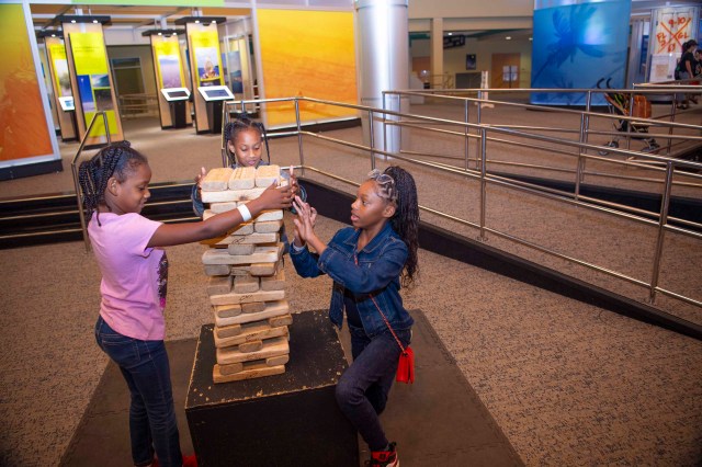 Three young visitors take turns removing pieces of wood from the giant-size blocks puzzle.