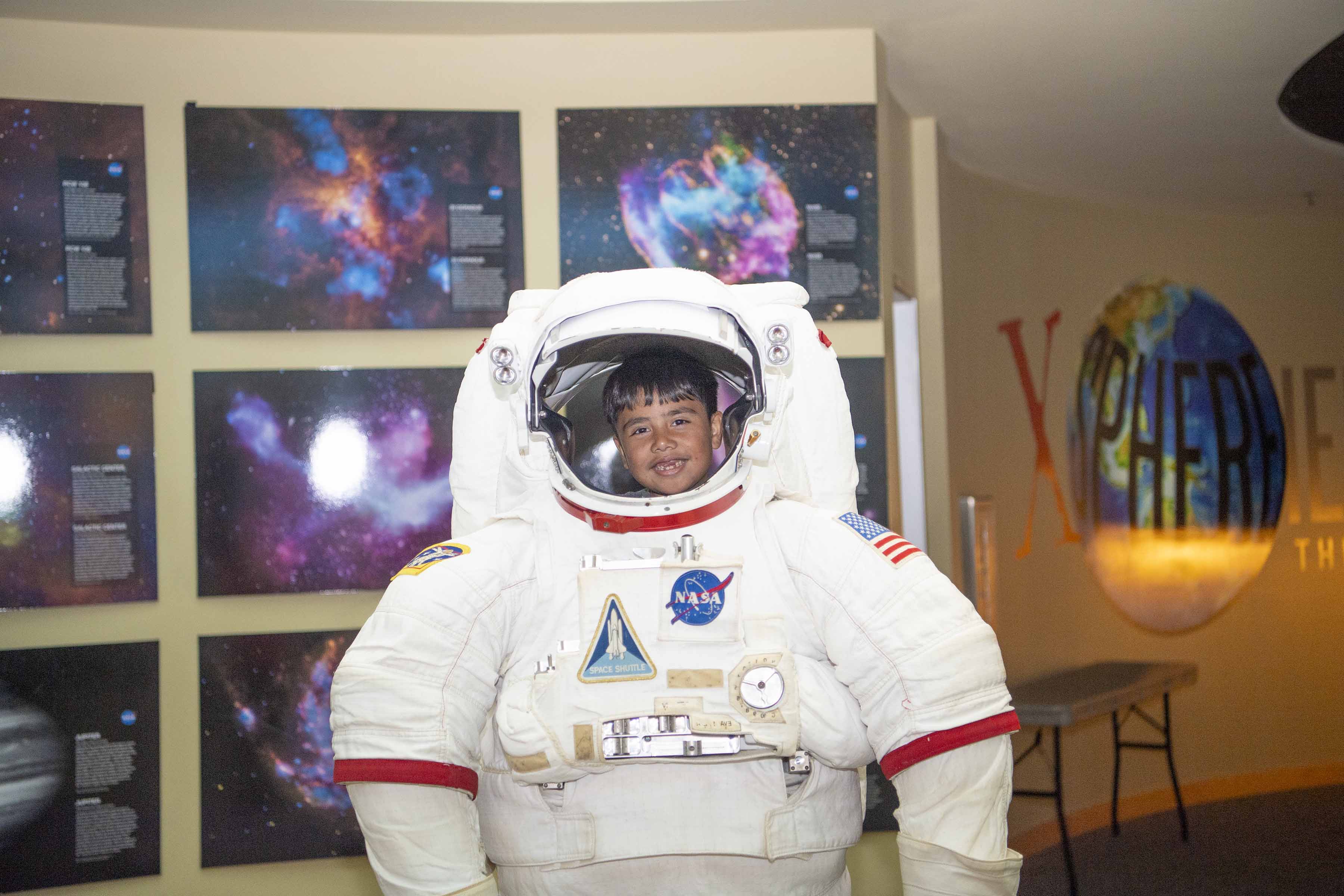 Young visitor poses for a picture while trying out the astronaut suit at INFINITY Science Center.