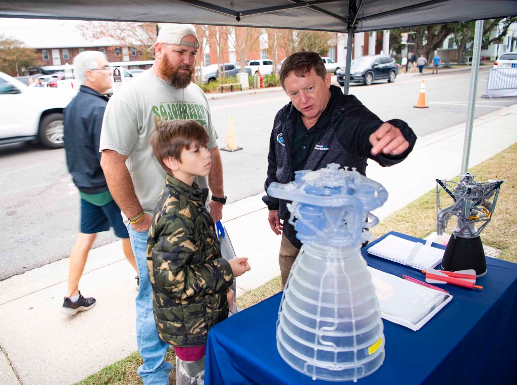 A few people gather to admire a 3-D model of engine.