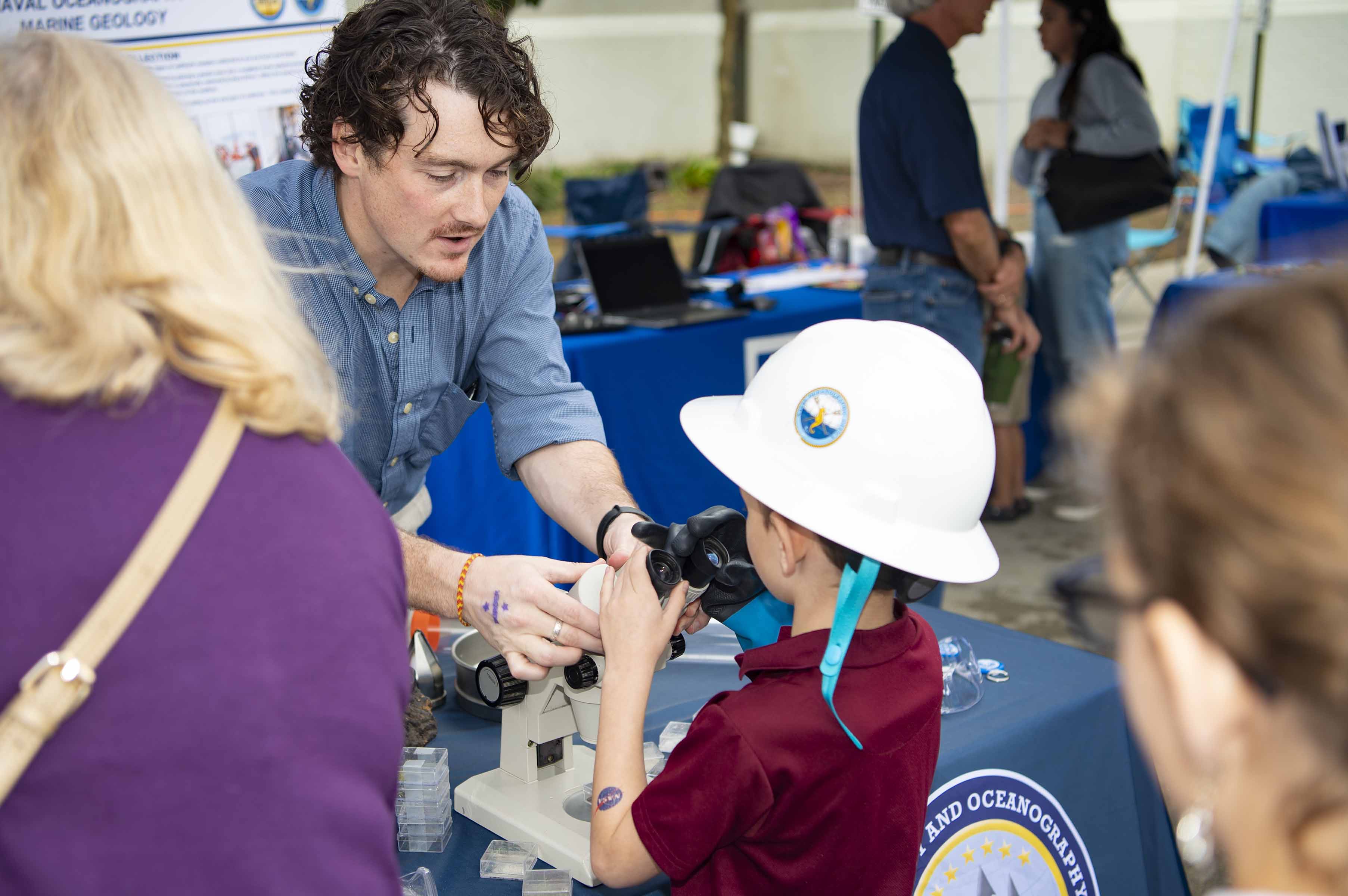 Young attendee at Stennis Day in the Bay looks through microscope at NAVO table.