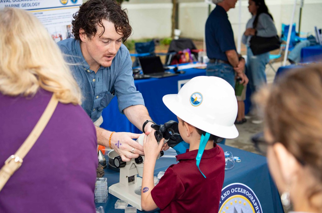 Young attendee at Stennis Day in the Bay looks through microscope at NAVO table.