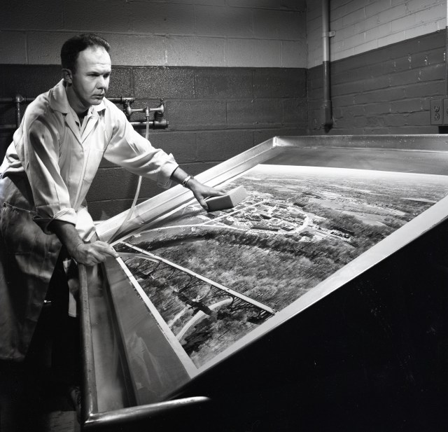 Man in darkroom working on oversized photograph.