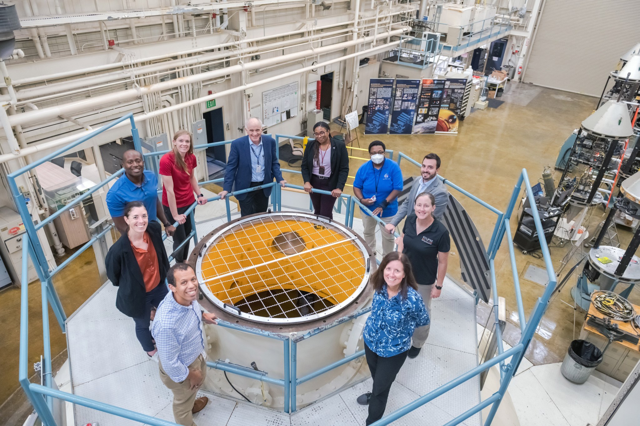 Alt Text: A group of Astronaut Candidates and NASA staff gather around a screened-in top of the vacuum chamber in the Zero Gravity Research Facility.