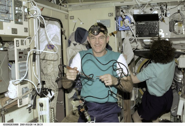 Astronaut James S. Voss, Expedition Two flight engineer, prepares to use a soldering tool for a maintenance task in the Zvezda Service Module onboard the International Space Station (ISS). Astronaut Susan J. Helms, flight engineer, is in the background. The image was recorded with a digital still camera.