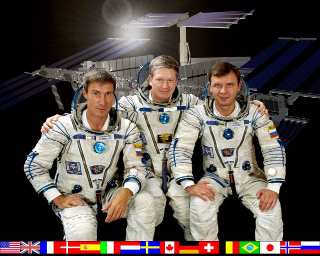 ISS Expedition One Commander William M. (Bill) Shepherd (center) is flanked by Soyuz Commander Yuri P. Gidzenko (right) and Flight Engineer Sergei K. Krikalev (left) in this crew photograph, taken during a break in training in Russia. The three, posed in front of a rendition of the International Space Station, are wearing the Sokol space suits like those they will don for their Soyuz-provided trip to ISS later this month. National flags representing all the international partners run along the bottom of the portrait.