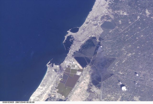 This Nadir view of Alexandria, Egypt, was provided by a digital still camera image down linked from the International Space Station to flight controllers in Houston. Alexandria (Al Iskandariya) occupies a T-shaped peninsula and strip of land separating the Mediterranean from Lake Mariout. According to NASA scientists studying the Expedition 1 photo collection, the town was originally built upon a mole (stone breakwater) called Heptastadium, which joined the island of Pharos to the mainland. Since then, the scientists say, sedimentary deposits have added considerably to the width of the mole. Since 1905, when the city’s 370 thousand inhabitants lived in an area of about four square kilometers between the two harbors, the city (population 4 million) has grown beyond its medieval walls and now occupies an area of about 300 square kilometers. The Mahmudiya Canal, connecting Alexandria with the Nile, runs to the south of the city and, by a series of locks, enters the harbor of the principal port of Egypt (note ships). The reddish and ochre polygons west of Lake Mariout are salt-evaporation, chemical-storage, and water-treatment ponds within the coastal lagoon.