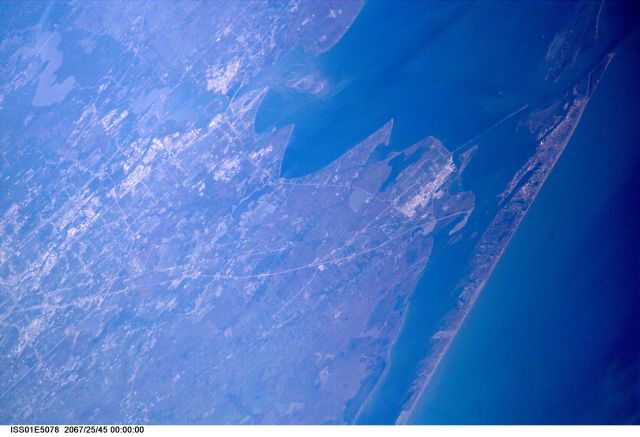 A northwesterly-looking view from over the Gulf of Mexico reveals much of Galveston and Harris Counties, as photographed with a digital still camera from the Earth-orbiting International Space Station (ISS). Galveston Island and Galveston Bay take up most of the right side of the frame, with parts of southern Harris County and even part of north Harris County, including Lake Houston, are visible on the left side of the frame. The Texas City Dike is in the upper right quadrant of the image.