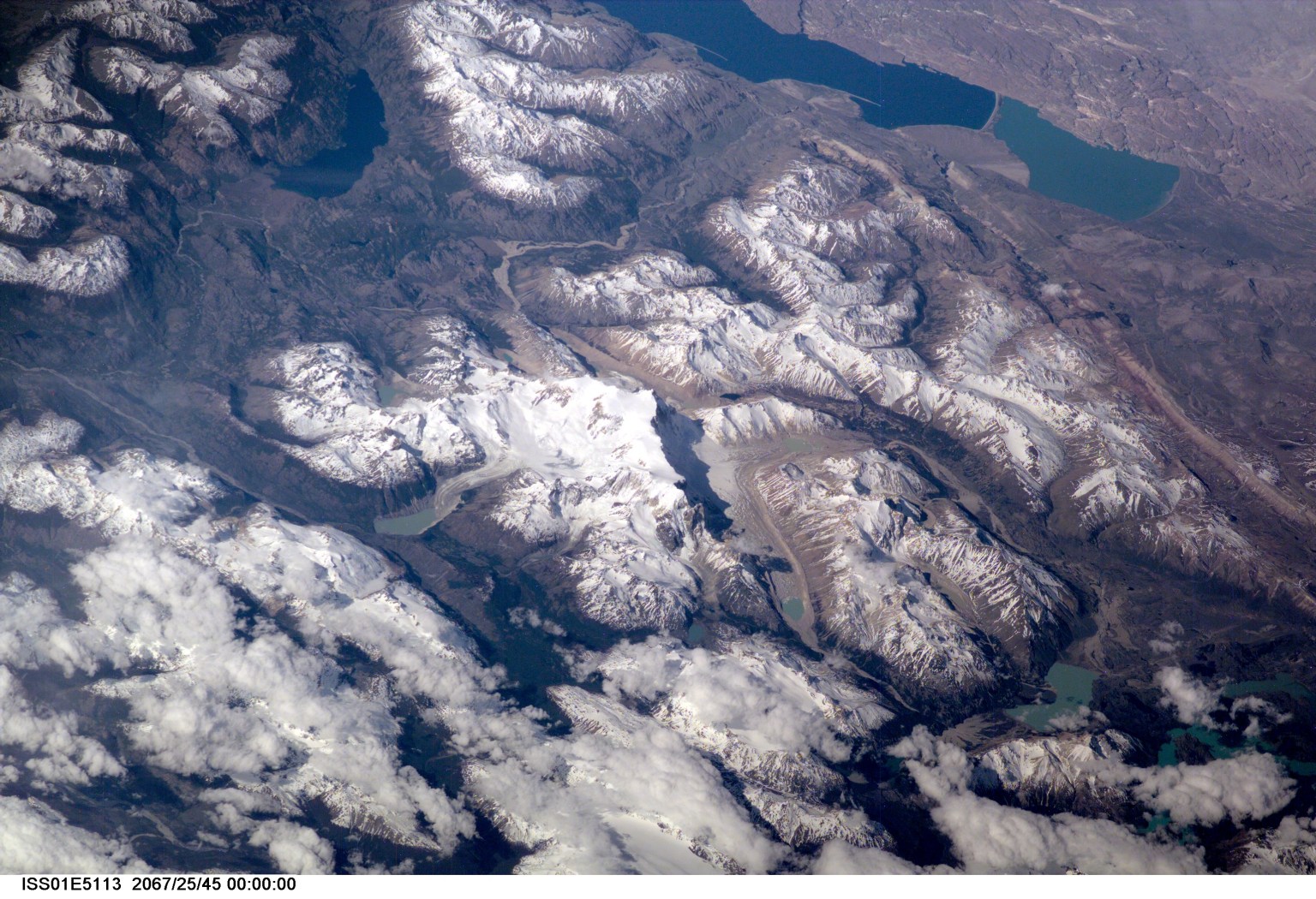 This scene on the remote, rugged Argentine/Chilean border in the far southern Andes Mountains offers numerous, dramatic examples of both erosional processes and features of ice and water. The sharp, glaciated crest of the Cerro San Lorenzo (center) exceeds 12,000 feet and casts a long shadow southeastward. Glaciers on its western flank flow into the valley. Lago Pueyrredon, and the other lakes visible here, have been excavated by geologically "recent" episodes of glacier erosion, when glaciers extended all the way onto the lowland plains (top right). Since the last melting of the glaciers, scientists estimate about 15,000 years ago, three distinct "fan-deltas" have formed where rivers flow into the lake. Counterclockwise currents in the lake, driven by strong winds from the west, have generated thin sand spits from each fan-delta. The largest spit (attached to the largest fan-delta, see right arrow) has isolated an approximately 10-kilometer long segment of the south end of the lake. This river, which has constructed the large fan, presently discharges turbid water to this isolated basin, giving it a lighter color than the rest of the lake. This Digital Still Camera photo was taken from the International Space Station, in December 2000 (late spring for this part of the world) when most of the previous winter's snow had melted below an altitude of 6,000 feet. Little evidence of man's presence can be found in this rough, desolate region. Glacial data collected over the past 50 years indicate that small ice bodies are disappearing at accelerated rates. (EOS, vol 81, no. 24, June 13, 2000) Predictions are that large fluctuations in land ice, with significant implications to society, are possible in the coming decades and centuries due to natural and anthropogenic climate change. Before glacial data can be used to address critical problems pertaining to the world's economic and environmental health, more detailed information about such glaciers is needed. Images like this from the International Space Station can be added to those taken from satellites (Landsat-7, instruments on the Terra satellite launched in 1999) to build data sets of glaciers in remote areas around the world.