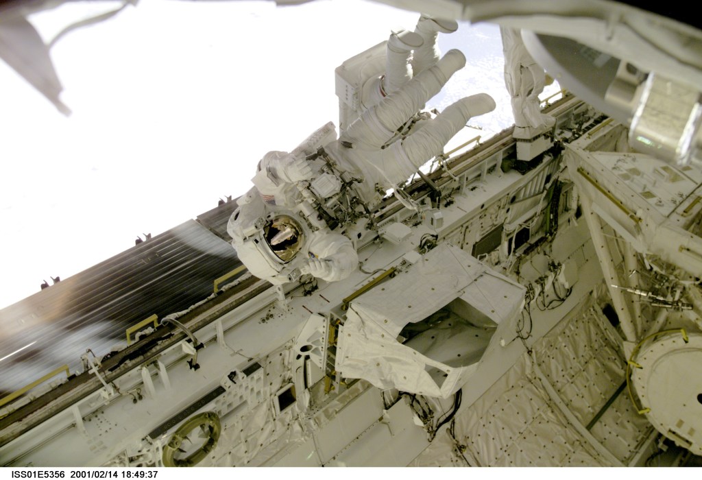 Astronaut Robert L. Curbeam, STS-98 mission specialist, floats above the longerons of the cargo bay on the Space Shuttle Atlantis during the final of three STS-98/5a space walks. Partially obscured behind Curbeam is astronaut Thomas D. Jones, his colleague and partner for all three walks. The scene was recorded with a digital still camera.