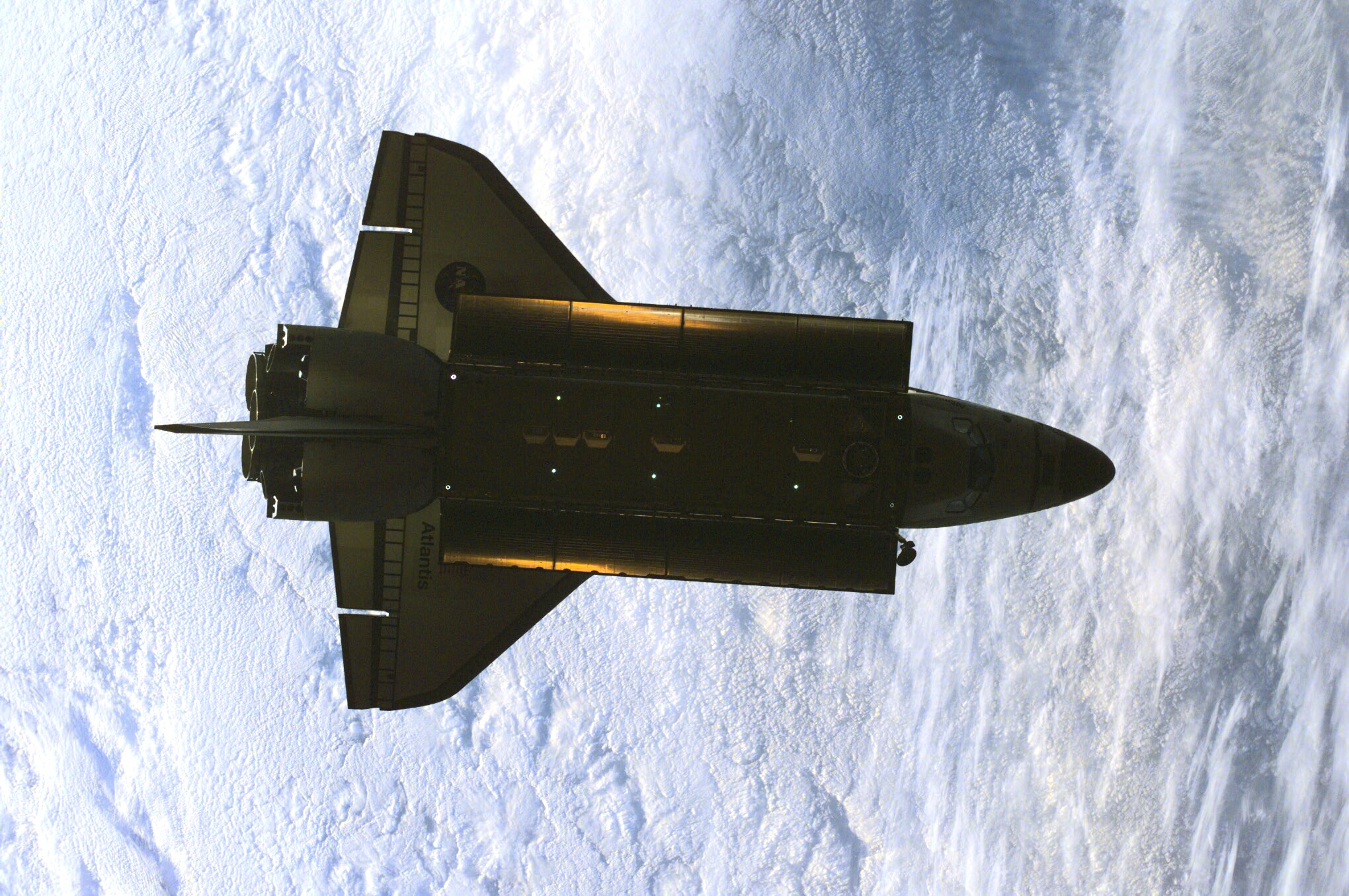 This partially silhouetted nadir image of the Space Shuttle Atlantis was photographed by the three-man Expedition One crew aboard the International Space Station (ISS) shortly after the shuttle and the outpost unlinked following several days of joint operations of the two crews. The scene, backdropped against a mass of white clouds on Earth, was recorded with a digital still camera.