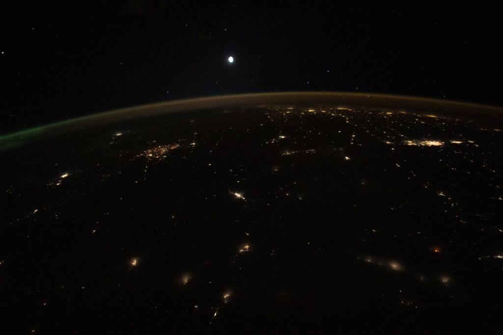 The Moon is pictured above Earth's horizon, its airglow, and an aurora (at far right) in this photograph from the International Space Station as it orbited 261 miles above the northwestern United States.