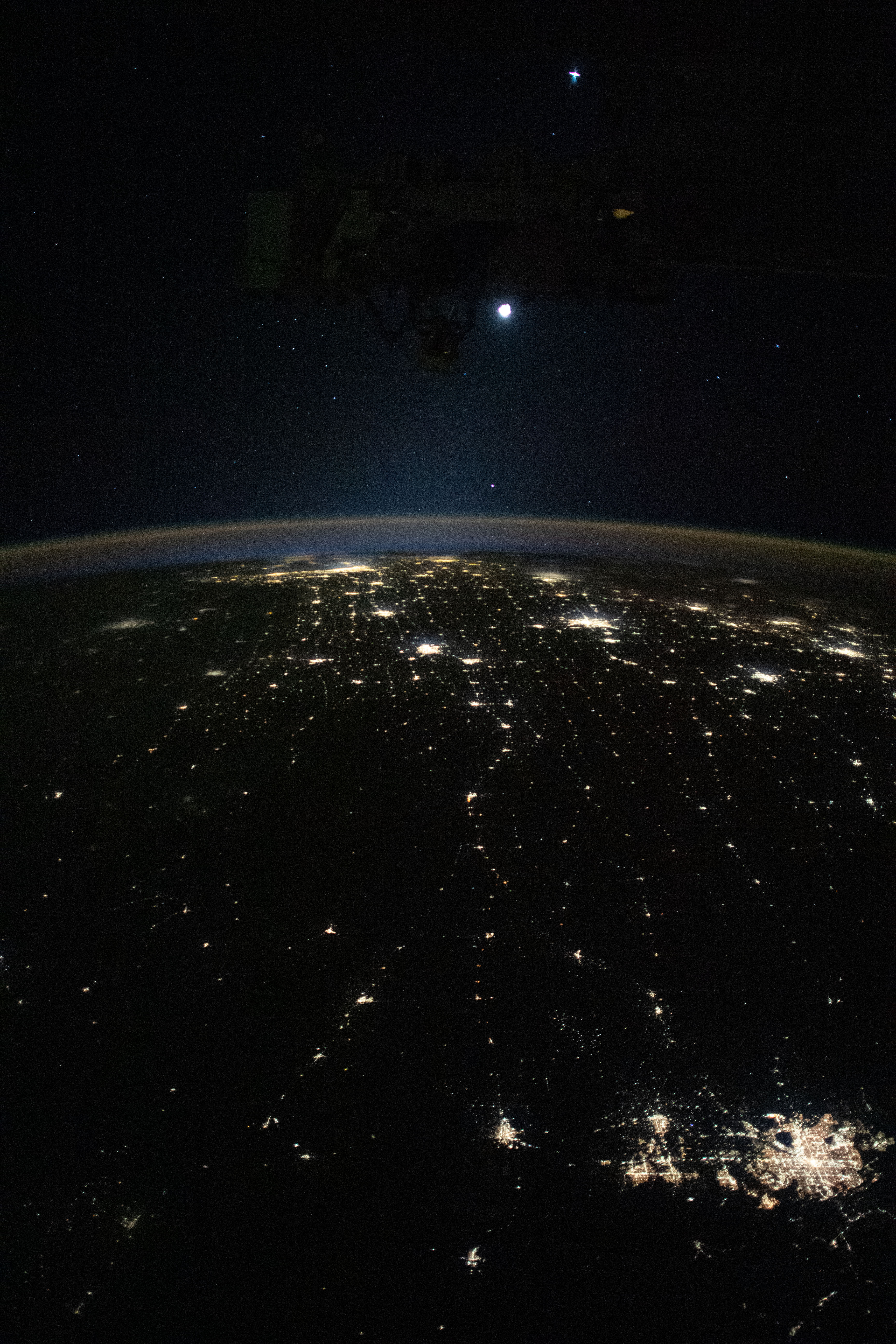 Earth's airglow outlines the planet's horizon with the Moon above in this photograph from the International Space Station as it orbited 260 miles above the midwestern United States. At lower right, the city lights of Denver. Colorado, and its suburbs shine, including the city lights all the way to Chicago, Illinois (at top), and surrounding metropolitan areas.