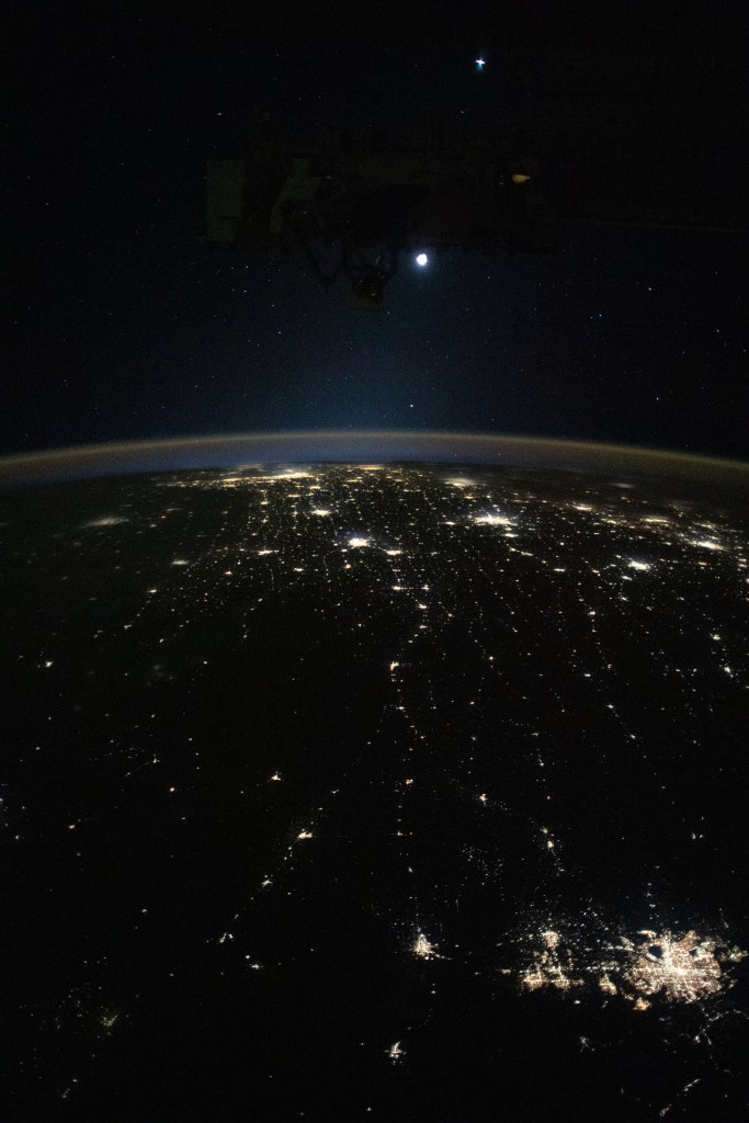 Earth's airglow outlines the planet's horizon with the Moon above in this photograph from the International Space Station as it orbited 260 miles above the midwestern United States. At lower right, the city lights of Denver. Colorado, and its suburbs shine, including the city lights all the way to Chicago, Illinois (at top), and surrounding metropolitan areas.