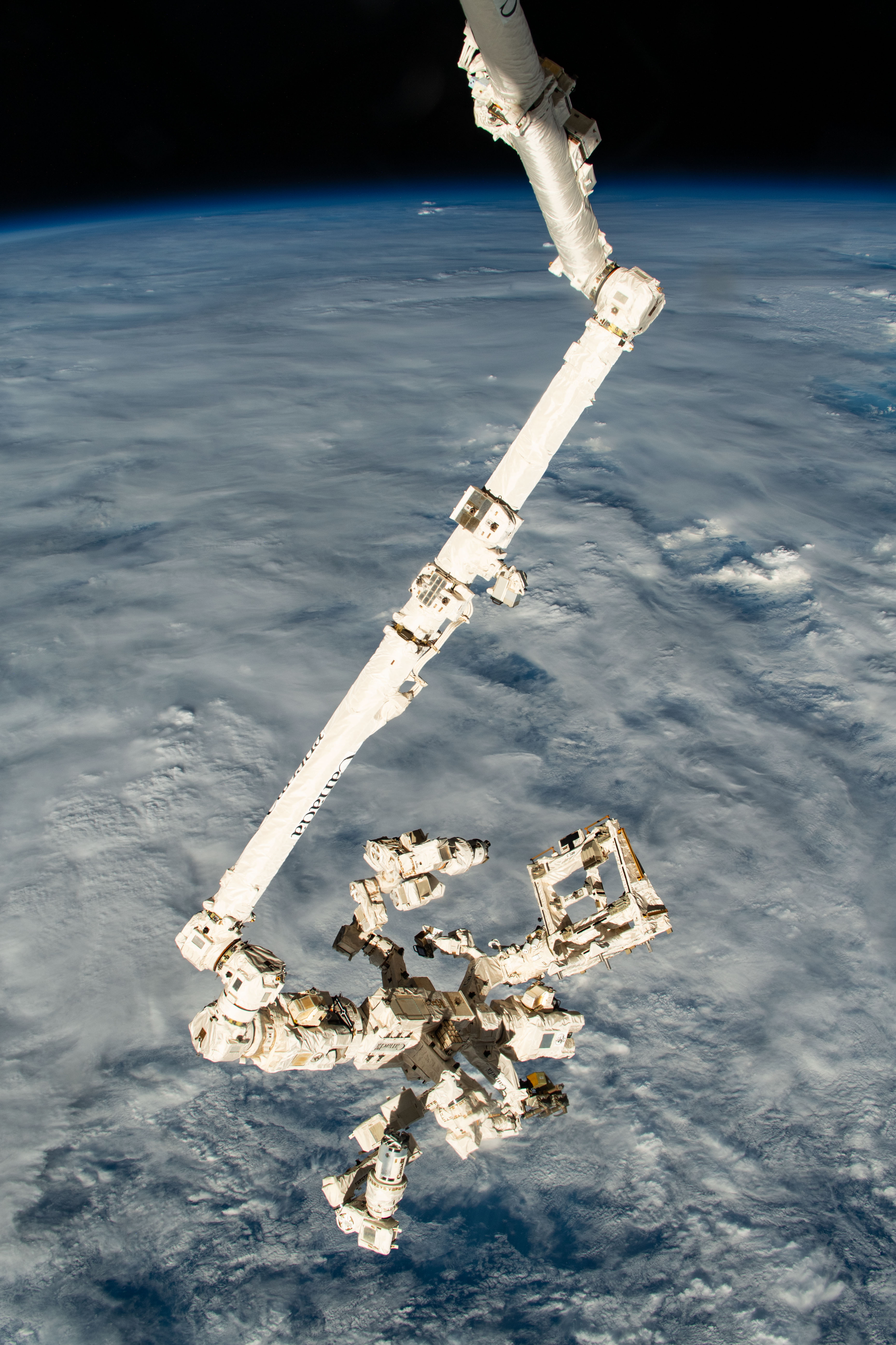 The Canadarm2 robotic arm with its fine-tuned robotic hand, also known as Dextre, attached extends vertically down from the International Space Station as it orbited 261 miles above a cloudy Pacific Ocean north of Papua New Guinea.