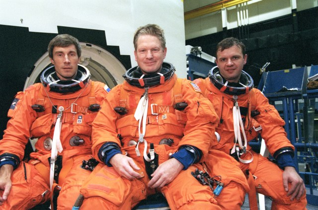 The ISS Expedition 1 crew takes a break from training in the systems integration facility at the Johnson Space Center for a crew photo. From the left are cosmonaut Sergei Krikalev, flight engineer; astronaut William Shepherd, mission commander; and cosmonaut Yuri Gidzenko, Soyuz commander. The trio is sitting on the hatch for one of the full-scale mockups used to prepare the crew for certain phases and contingencies of their shuttle return flight.