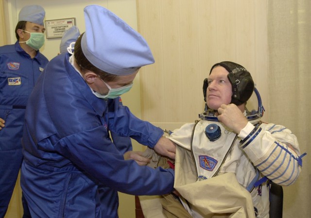 Expedition 1 commander William M. (Bill) Shepherd gets help with his Sokol suit prior to a simulation at Baikonur. Out of frame are Soyuz pilot Yuri P. Gidzenko and flight engineer Sergei K. Krikalev.