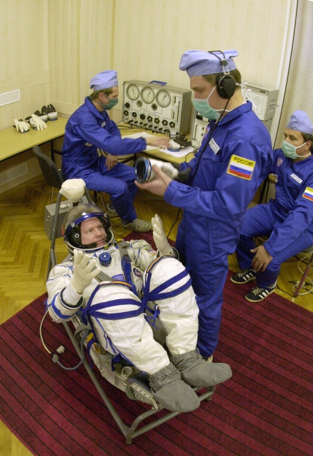 Expedition 1 commander William M. (Bill) Shepherd, wearing a Sokol suit, gets help with his glove before entering the Soyuz spacecraft at Baikonur. Out of frame are Soyuz pilot Yuri P. Gidzenko and flight engineer Sergei K. Krikalev.