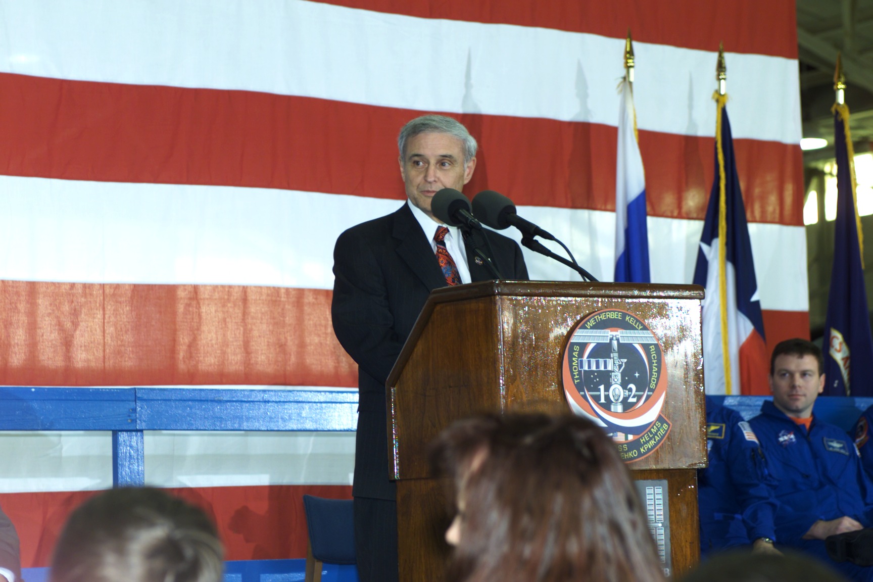 JSC Acting Director Roy S. Estess introduces the STS-102 and Expedition One crew members to a crowd gathered in Ellington Field's Hangar 990 during crew return ceremonies.