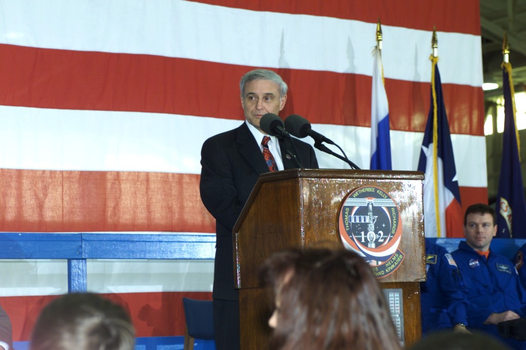 JSC Acting Director Roy S. Estess introduces the STS-102 and Expedition One crew members to a crowd gathered in Ellington Field's Hangar 990 during crew return ceremonies.