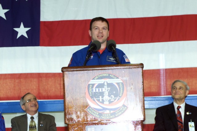 Astronaut James M. Kelly, STS-102 pilot, speaks to a crowd of greeters during a crew return ceremony in Ellington Field's Hangar 990. Pictured in the background on the dais are Joseph Rothenberg (left), NASA Associate Administrator for Space Flight, and Roy S. Estess, Johnson Space Center Acting Director.