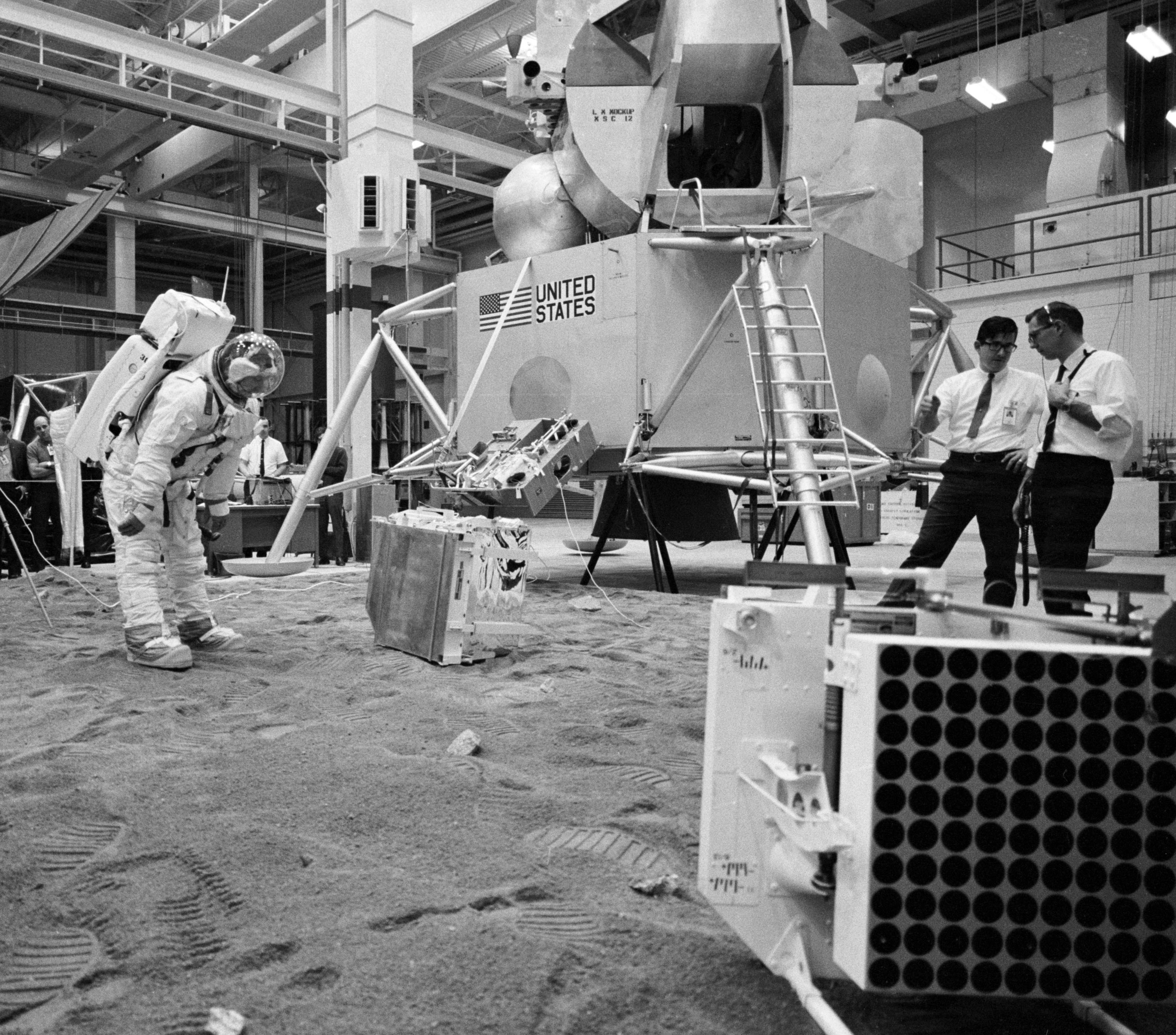A suited technician deploys mockups of the Apollo 11 experiments – the SWC, far left, the PSEP, and the LRRR, during a test session