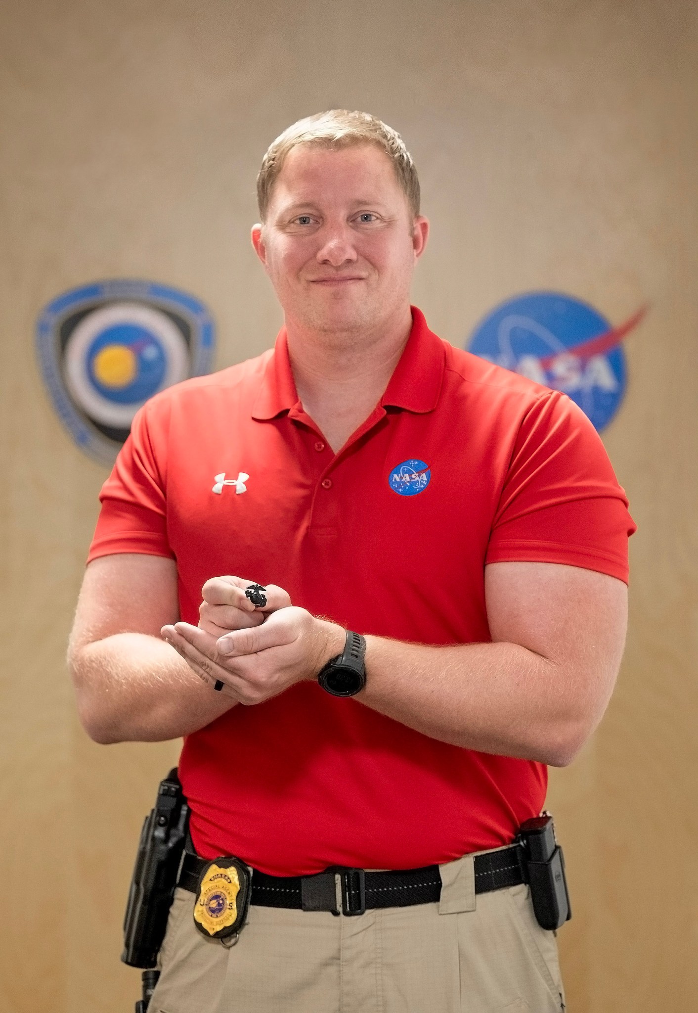 A white man in a red NASA shirt holds a military ring in front of him.