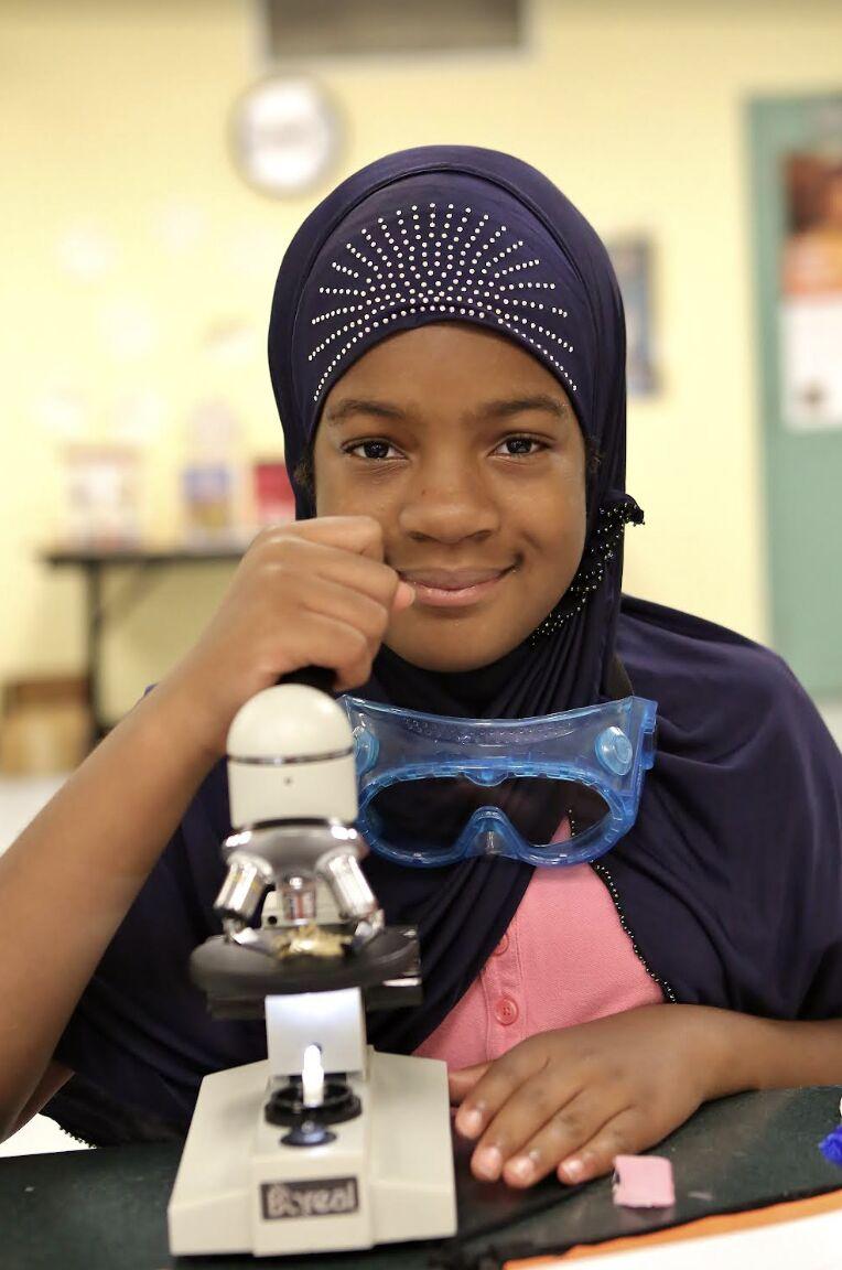 a young female child poses with a microscope