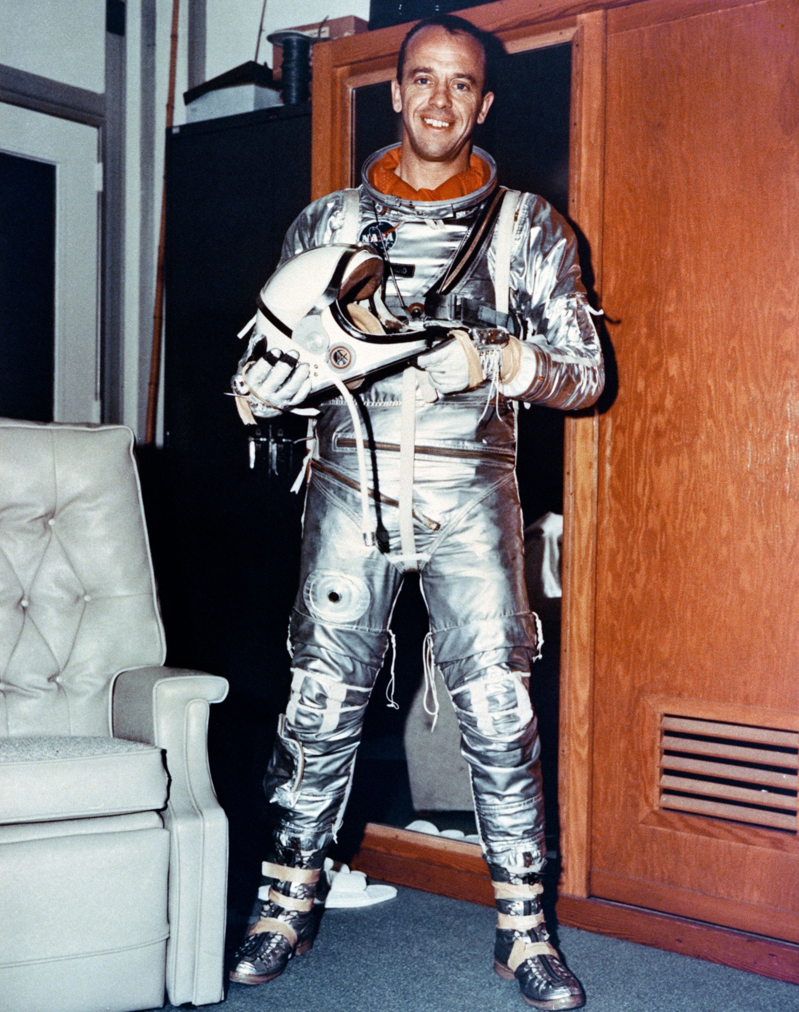 Astronaut Alan Shepard smiles while wearing an all-silver pressure suit for the Mercury mission. He holds a white helmet in his hands.