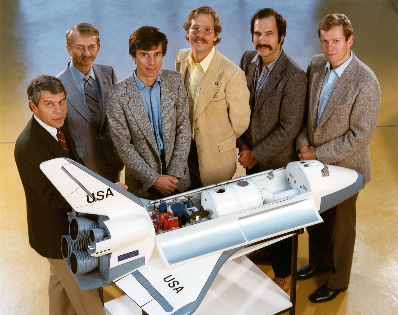 The mission specialists and payload specialists of STS-9 poses next to a model of the Space Shuttle