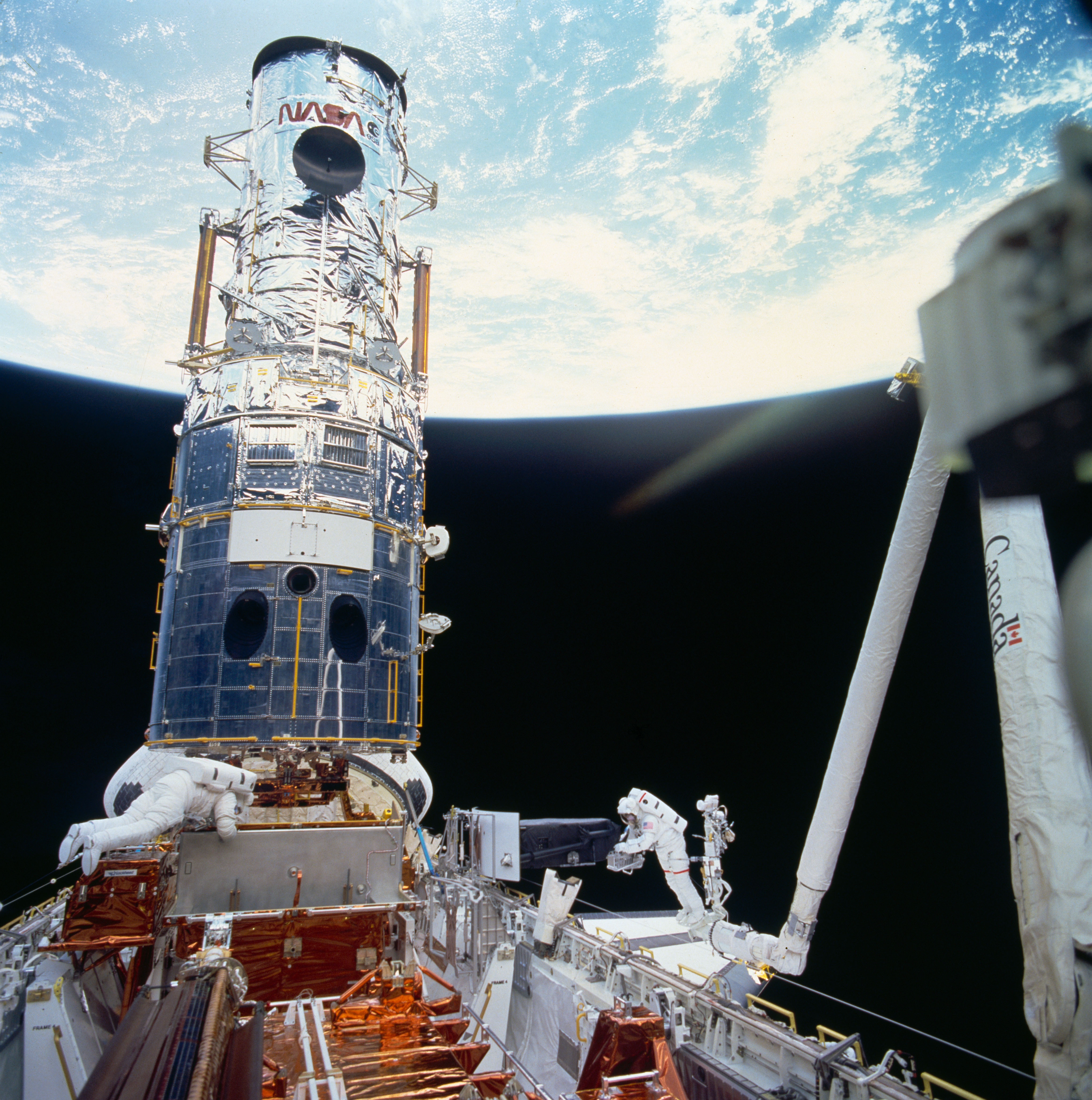 Musgrave, left, and Hoffman have installed WFPC2, the white triangle in the middle of the telescope, with Hoffman about to pick up WFPC1 temporarily stowed on the side of the payload bay and place it in its permanent location for return to Earth