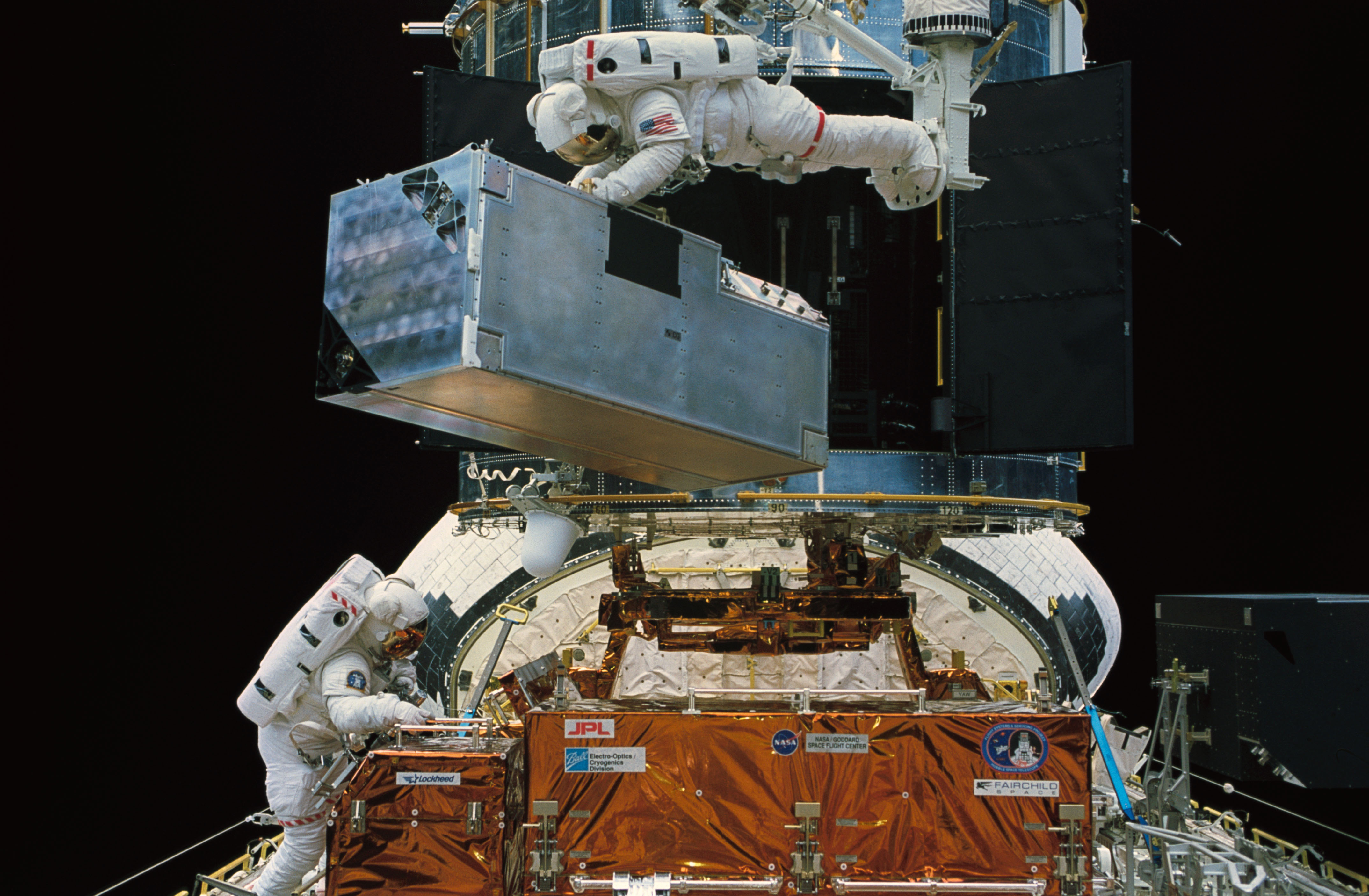 European Space Agency astronaut Claude Nicollier controlling the Remote Manipulator System, Thornton, top, removes the Corrective Optics Space telescope Axial Replacement (COSTAR) from its storage location