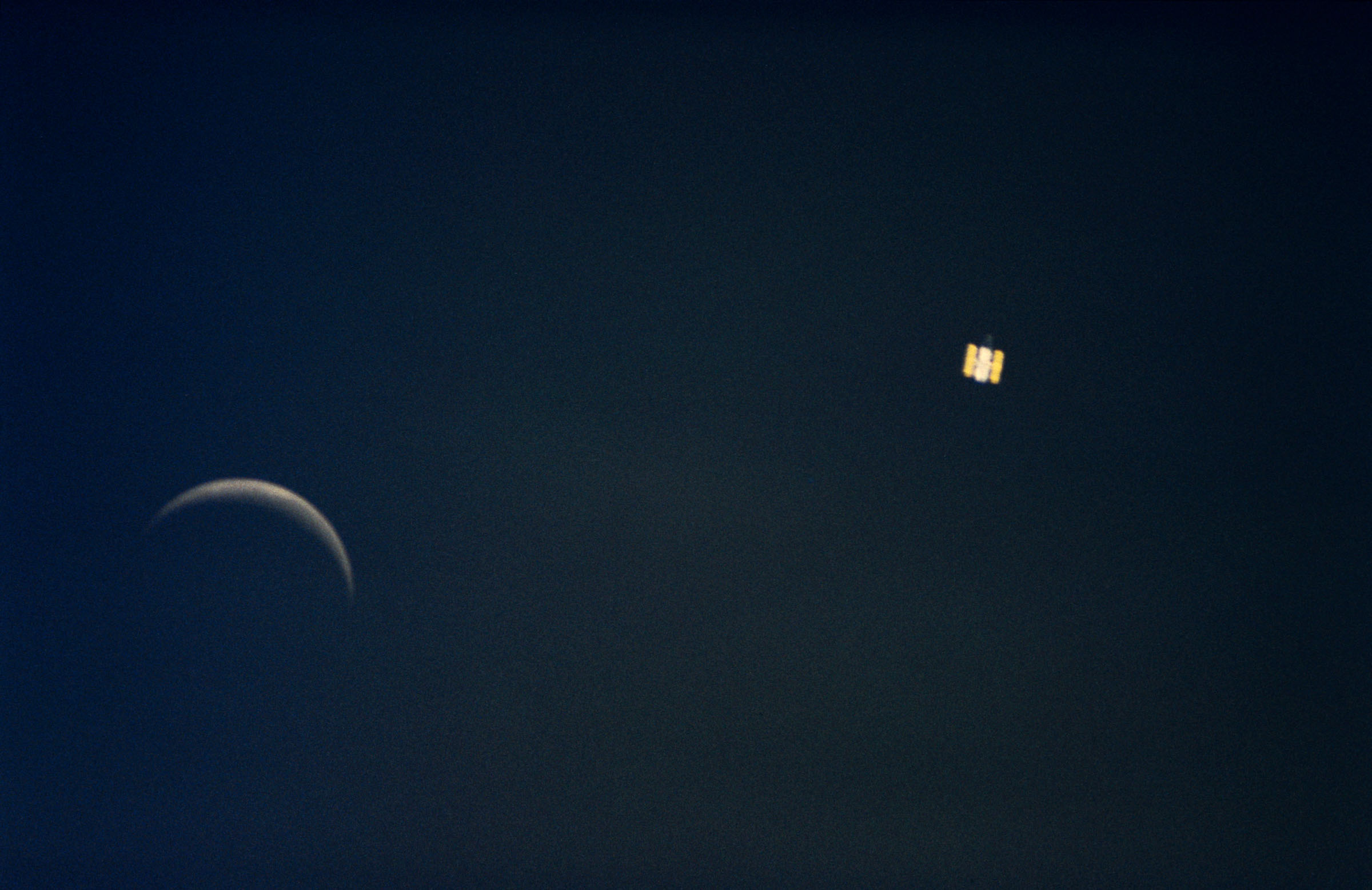 A distant view of Hubble, right, with a crescent Moon