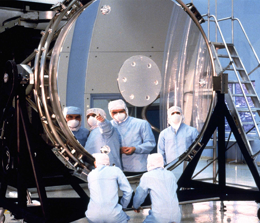 Workers inspect the Hubble Space Telescope’s 94-inch diameter primary mirror prior to assembly