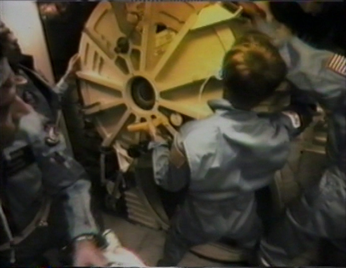 Several STS-9 crew members struggle to open the hatch to the transfer tunnel