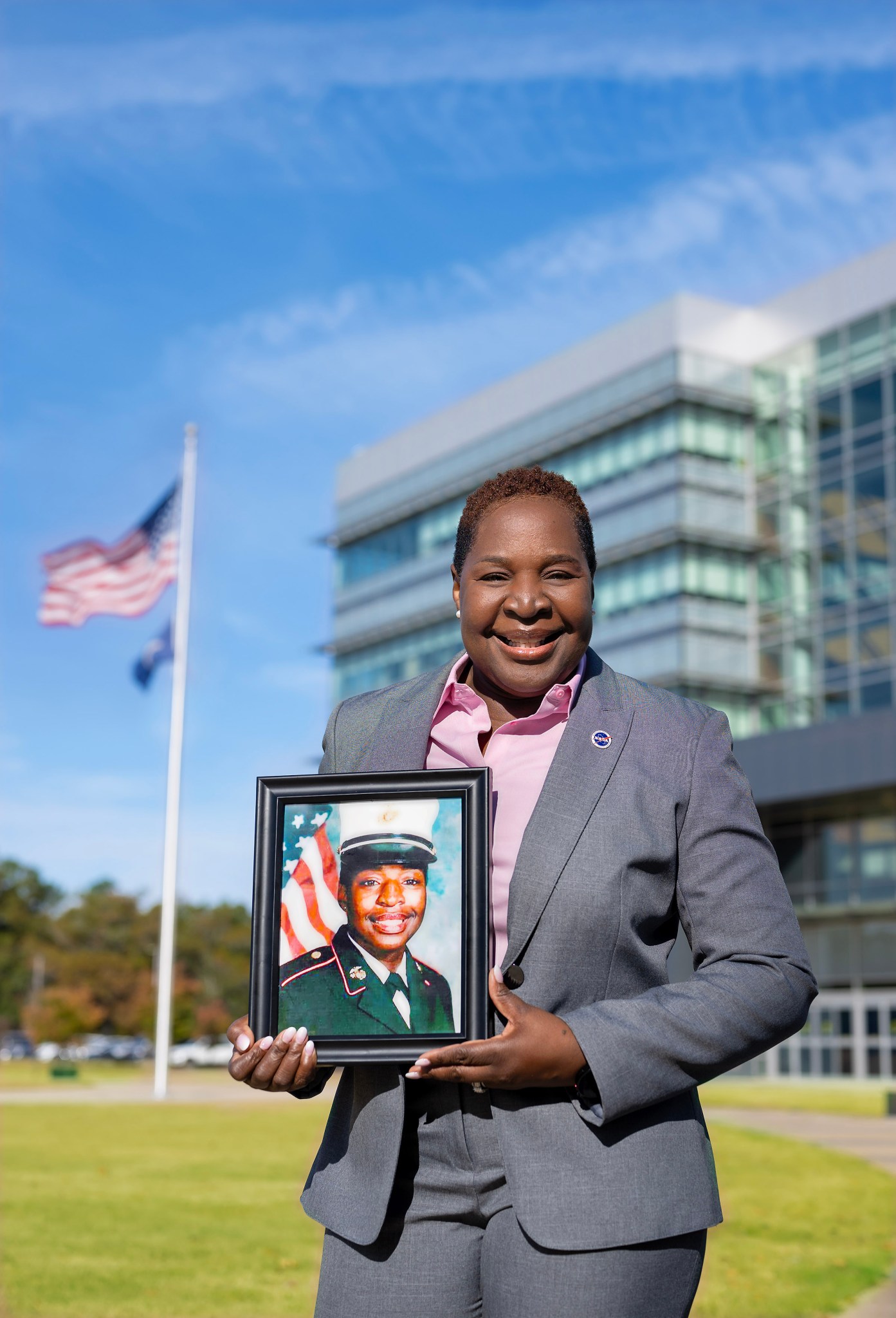 Tory Henry, a Black woman stands in front of Marshall Space Flight Center building 4221 holding her military photo with the American flag in the background.