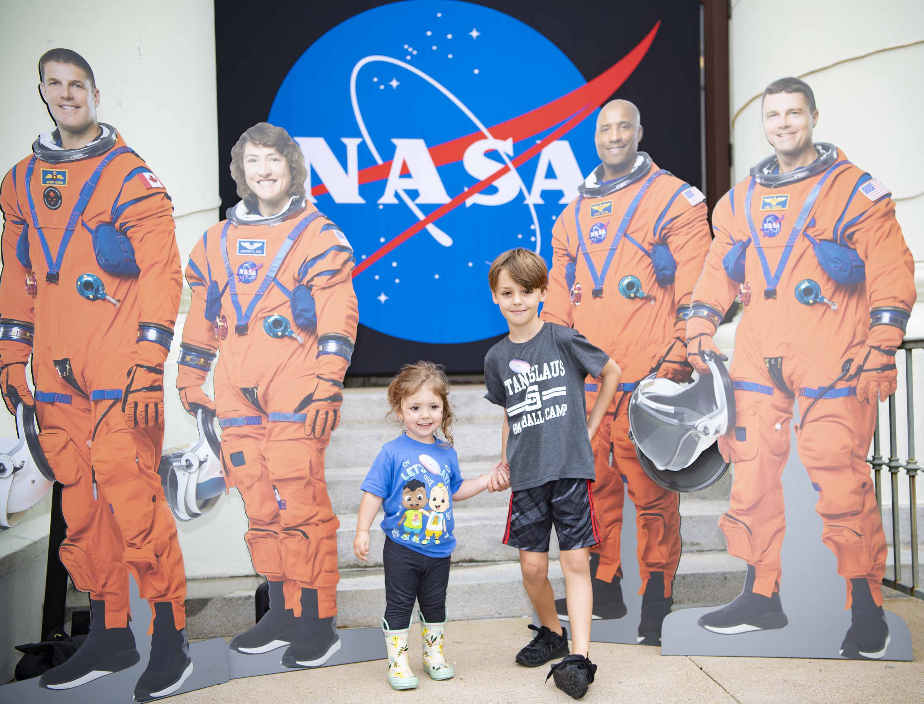 Two children stand with cutouts of the Artemis II crew