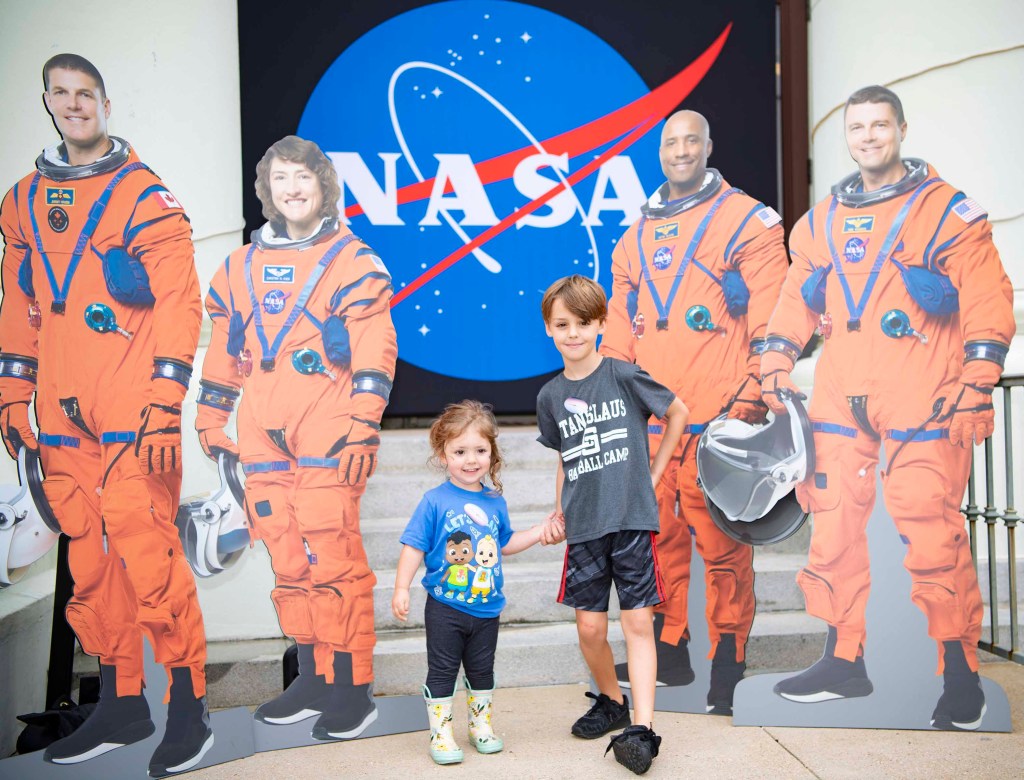 Two children stand with cutouts of the Artemis II crew