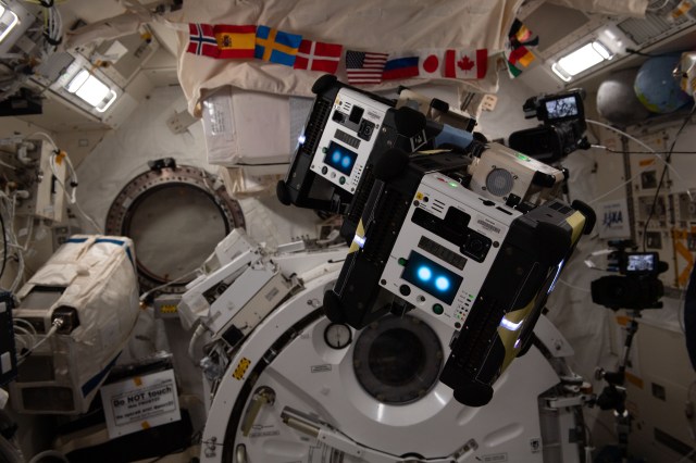 iss070e038773 (Dec. 13, 2023) --Two free-flying robotic helpers, Astrobee, float in microgravity. The robots are designed to help crews aboard the International Space Station complete daily tasks and reduce the time spent on routine duties.