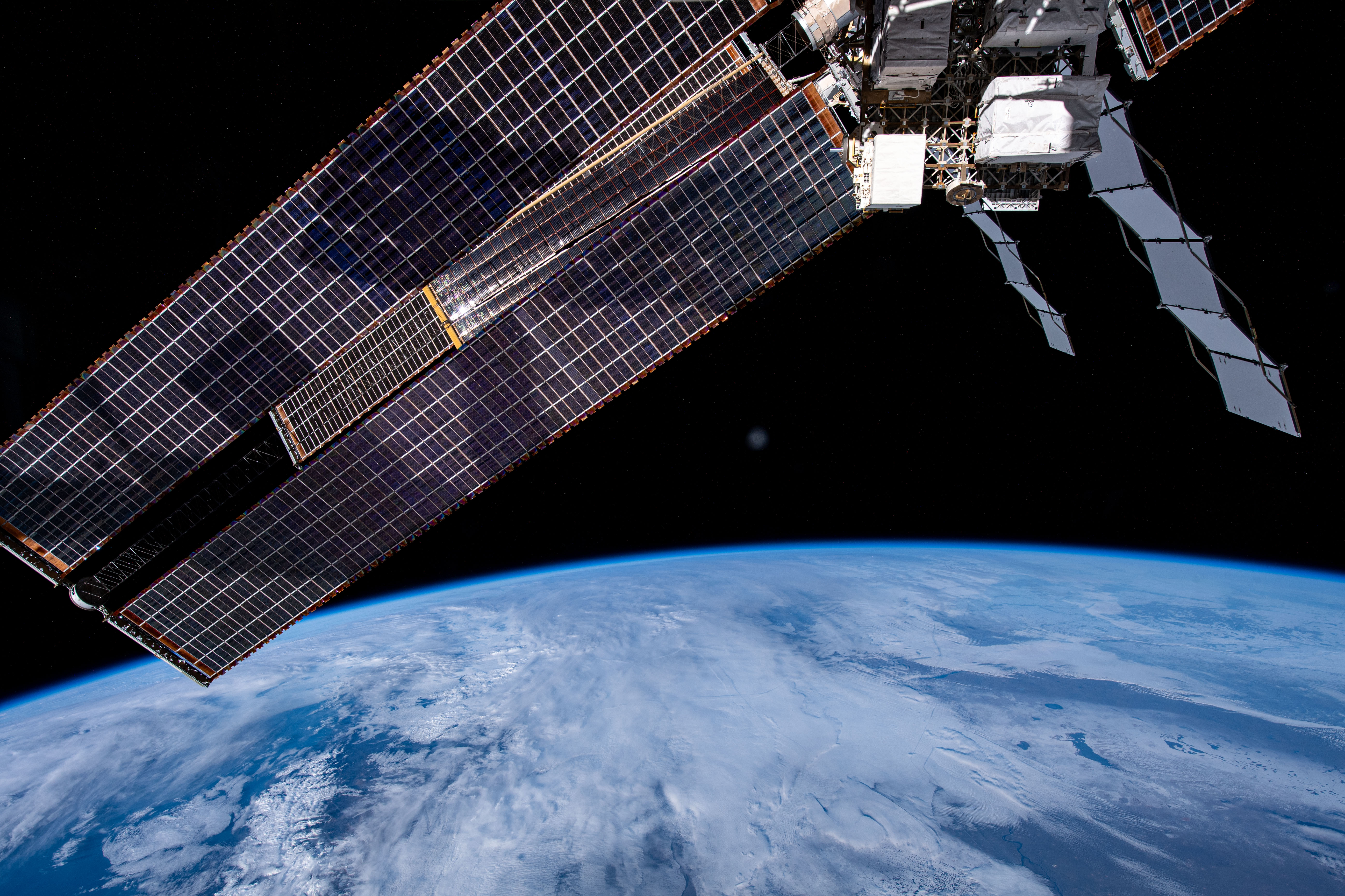 iss070e036961 (Dec. 8, 2023) -- As the International Space Station soared 260 miles above the Middle East, the blue glow of Earth is met with clouds hanging overhead. Above it, exterior station hardware and one of the orbital lab's roll-out solar arrays can be seen.