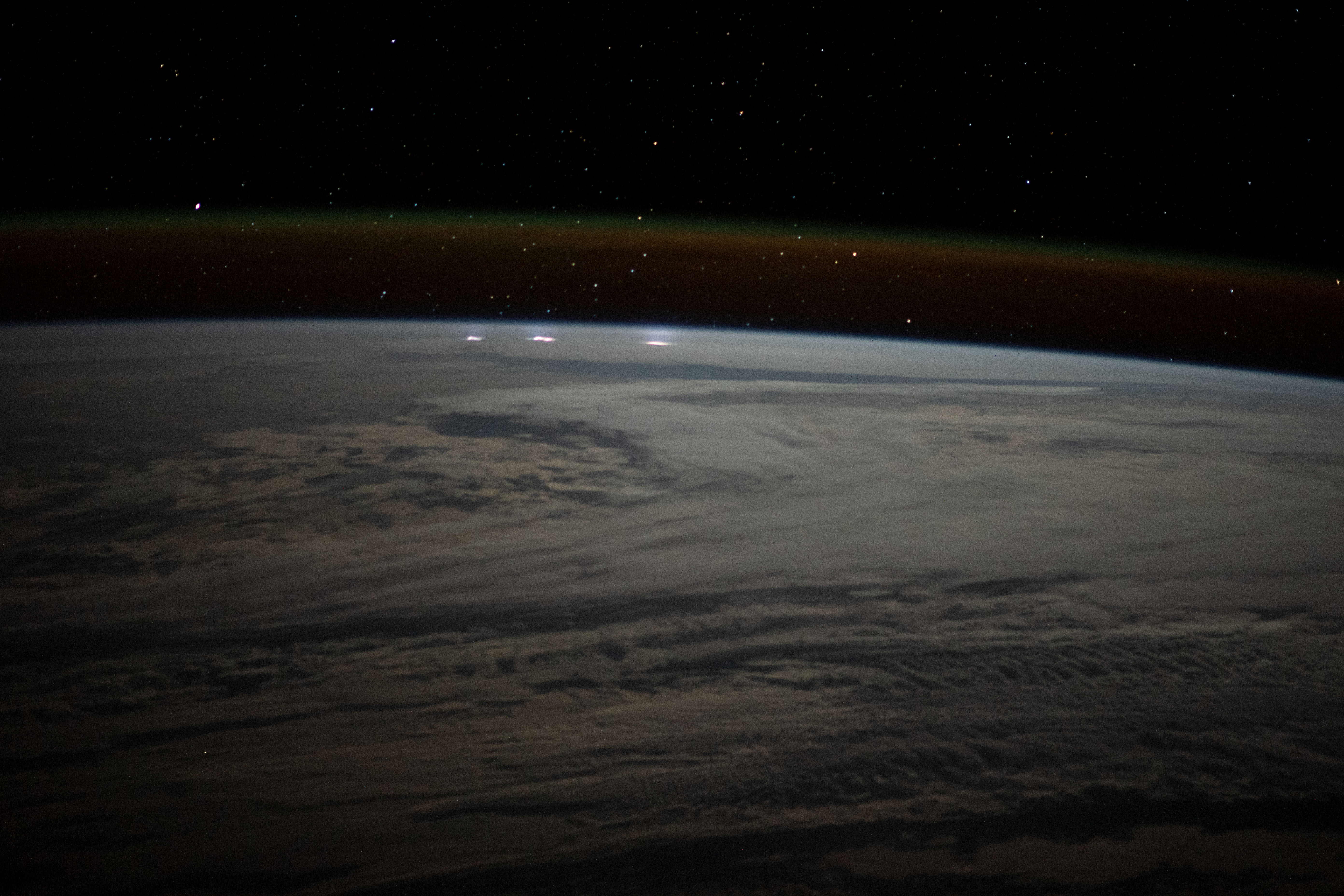 A cloudy, south Indian Ocean between Africa and Antarctica, with lightning storms near the horizon beneath the atmospheric glow, is pictured from the International Space Station as it orbited 271 miles above